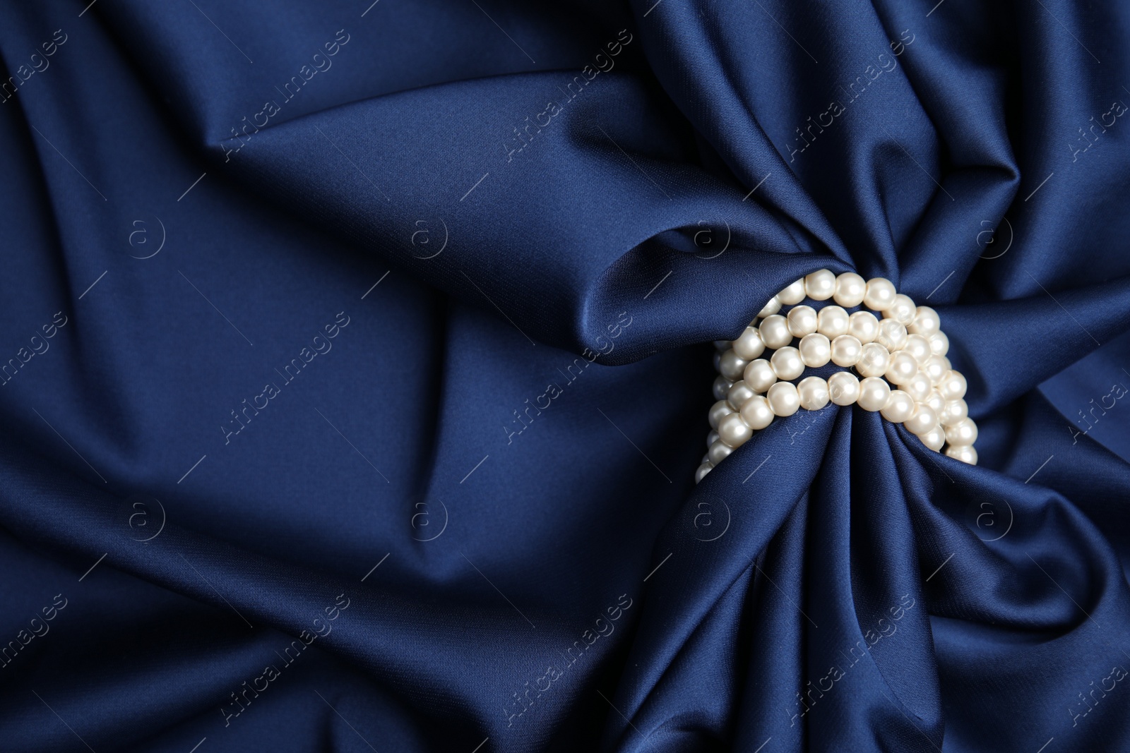 Photo of Beautiful pearls with dark blue silk as background, space for text