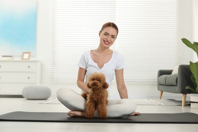 Photo of Happy young woman practicing yoga on mat with her cute dog at home