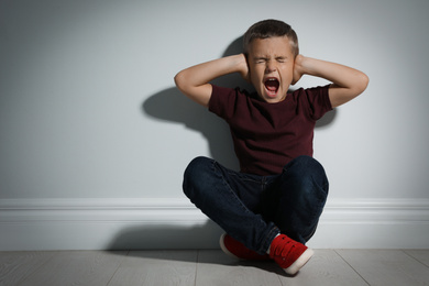 Scared little boy near white wall. Domestic violence concept