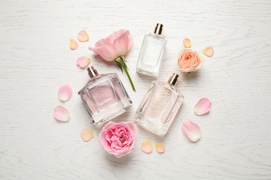 Photo of Flat lay composition with different perfume bottles and roses on white wooden background