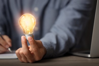 Photo of Glow up your ideas. Closeup view of man holding light bulb while working at desk, space for text