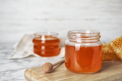 Photo of Glass jar with sweet honey and dipper on wooden board