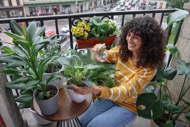 Beautiful young woman spraying potted houseplants with water on balcony