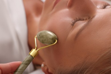 Woman receiving facial massage with jade roller in beauty salon, closeup