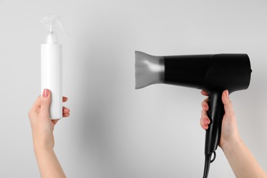 Photo of Woman holding spray bottle with thermal protection and hairdryer on white background, closeup