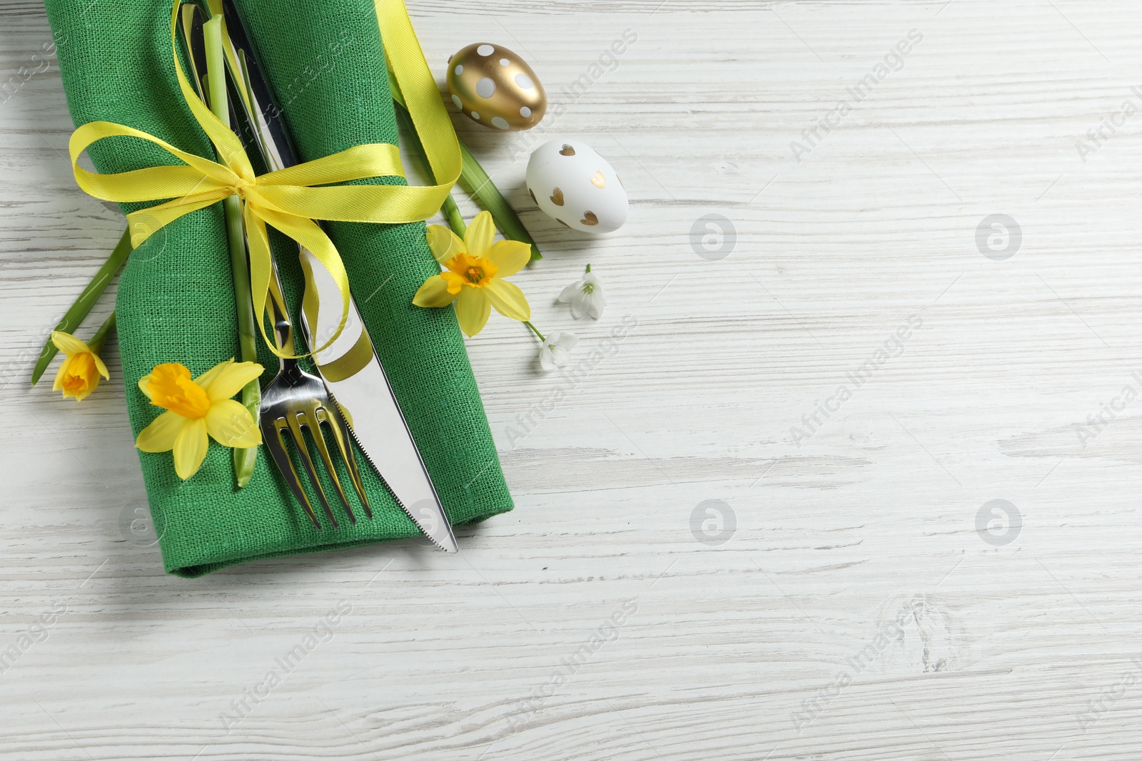 Photo of Cutlery set, Easter eggs and narcissuses on white wooden table, flat lay. Space for text