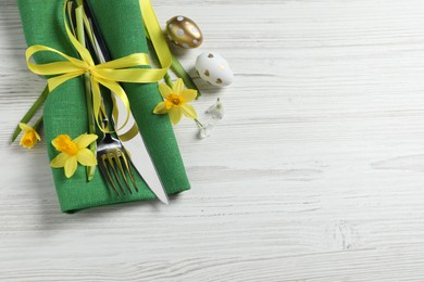 Cutlery set, Easter eggs and narcissuses on white wooden table, flat lay. Space for text