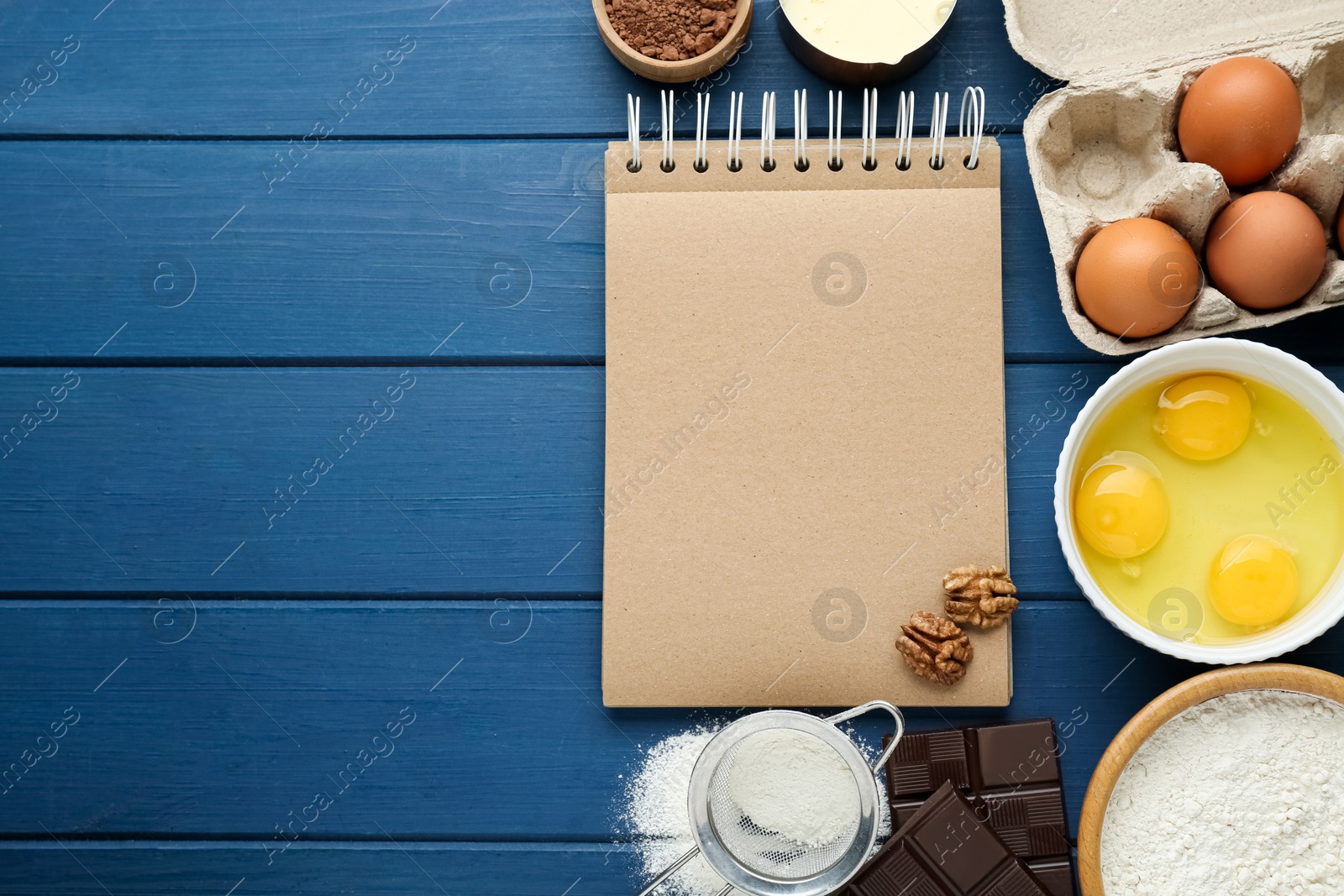 Photo of Blank recipe book and different ingredients on blue wooden table, flat lay. Space for text