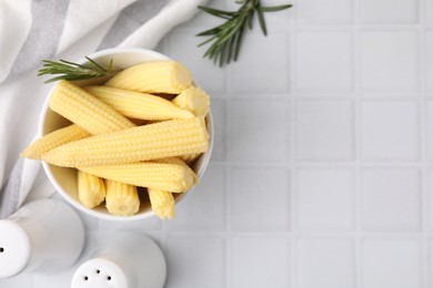 Photo of Tasty fresh yellow baby corns in bowl on white tiled table, top view. Space for text