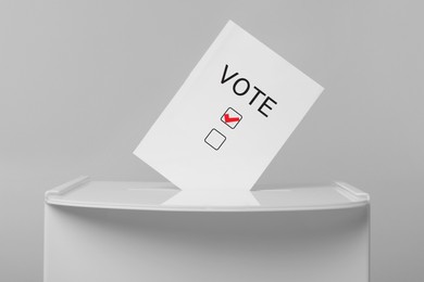 Paper with word Vote and tick sticking out of ballot box on light grey background