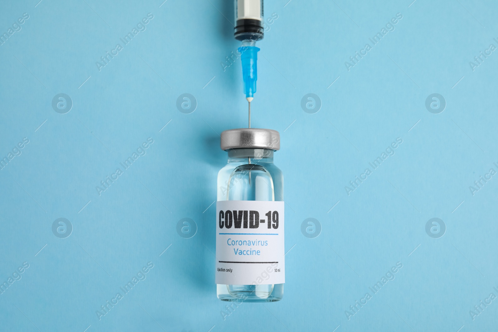 Photo of Filling syringe with coronavirus vaccine on light blue  background, flat lay