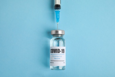 Photo of Filling syringe with coronavirus vaccine on light blue  background, flat lay