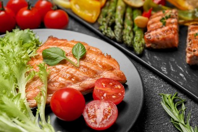Tasty grilled salmon with tomatoes and fresh lettuce on black table, closeup. Space for text