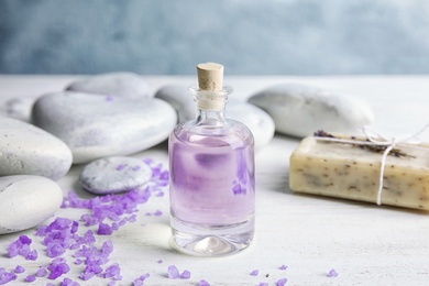 Photo of Bottle with natural herbal oil, soap and lavender flowers on table against blurred background