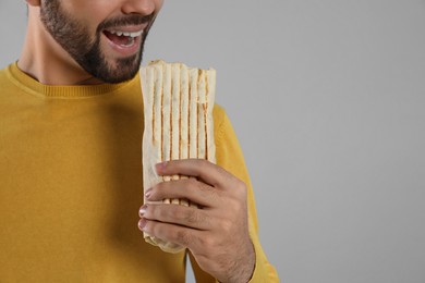 Young man eating tasty shawarma on grey  background, closeup. Space for text