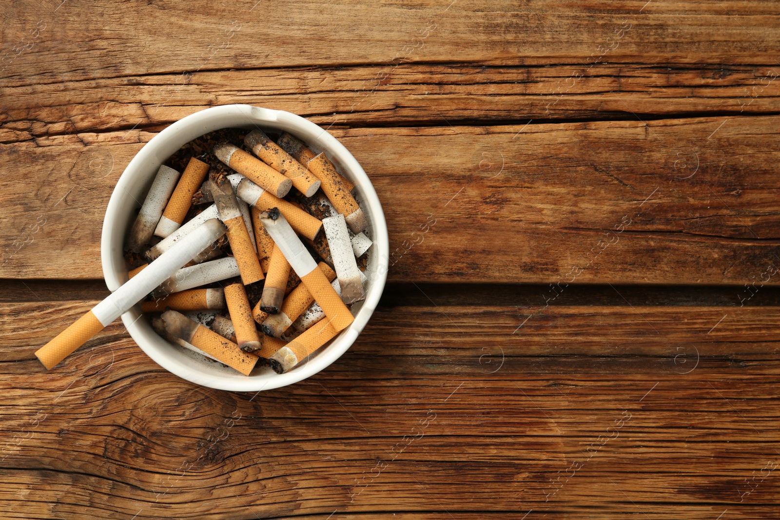 Photo of Ceramic ashtray full of cigarette stubs on wooden table, top view. Space for text