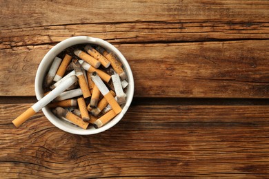 Photo of Ceramic ashtray full of cigarette stubs on wooden table, top view. Space for text