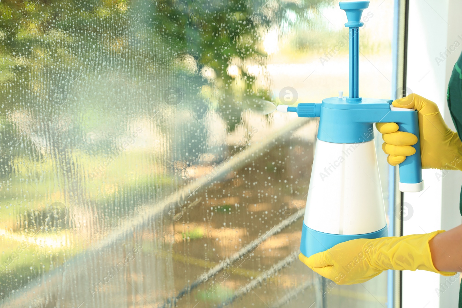 Photo of Janitor cleaning window with detergent indoors, closeup