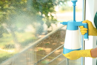 Photo of Janitor cleaning window with detergent indoors, closeup