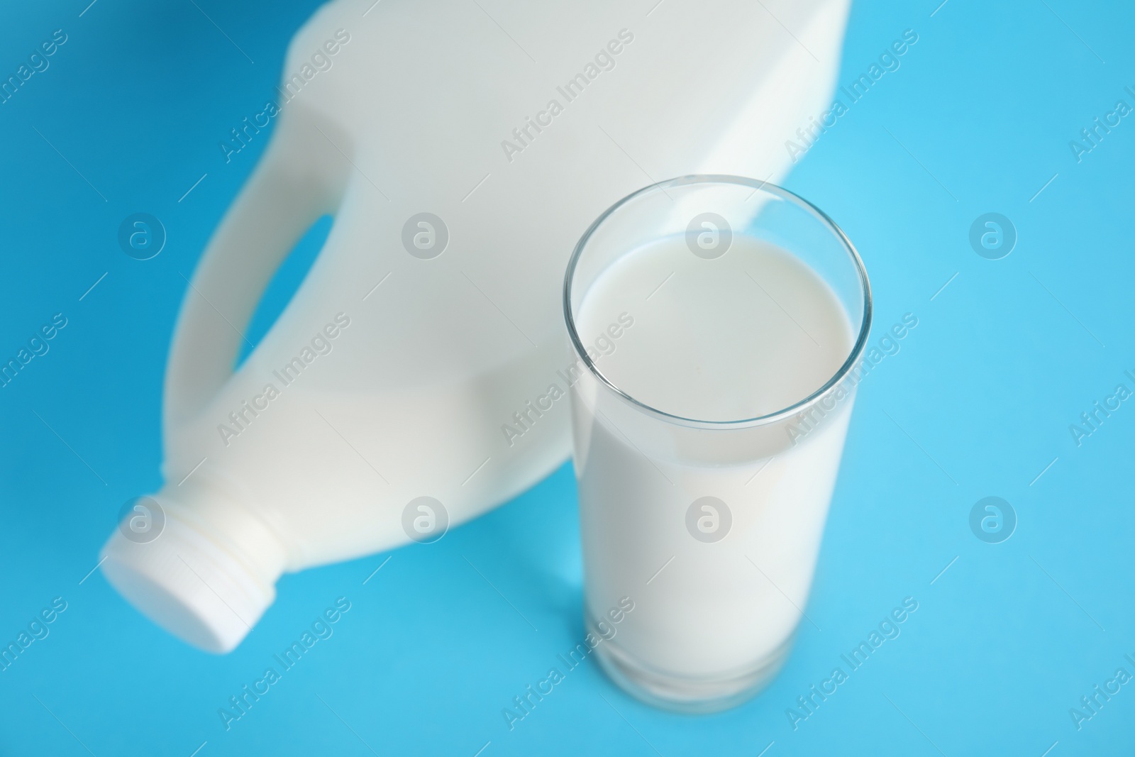 Photo of Gallon bottle of milk and glass on light blue background