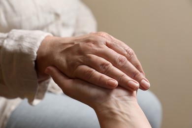 Photo of Woman holding hands with her mother on beige background, closeup