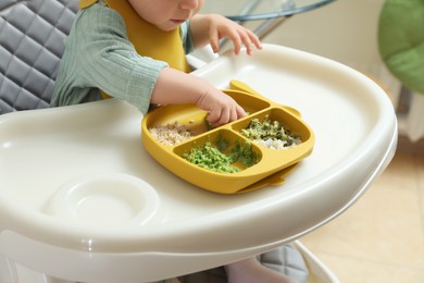 Photo of Little baby eating healthy food in high chair indoors, closeup