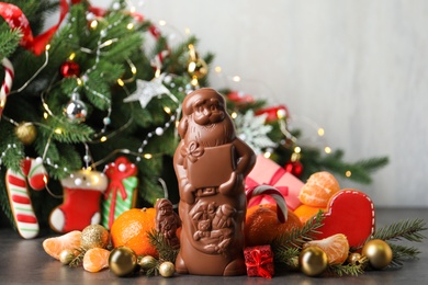 Composition with chocolate Santa Claus candies on grey table near Christmas tree