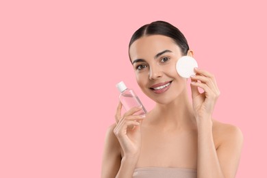 Photo of Beautiful woman removing makeup with cotton pad on pink background, space for text