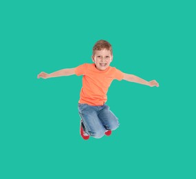 Happy boy jumping on dark turquoise background, full length portrait