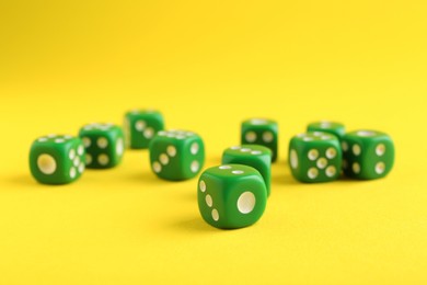 Photo of Many green game dices on yellow background, closeup