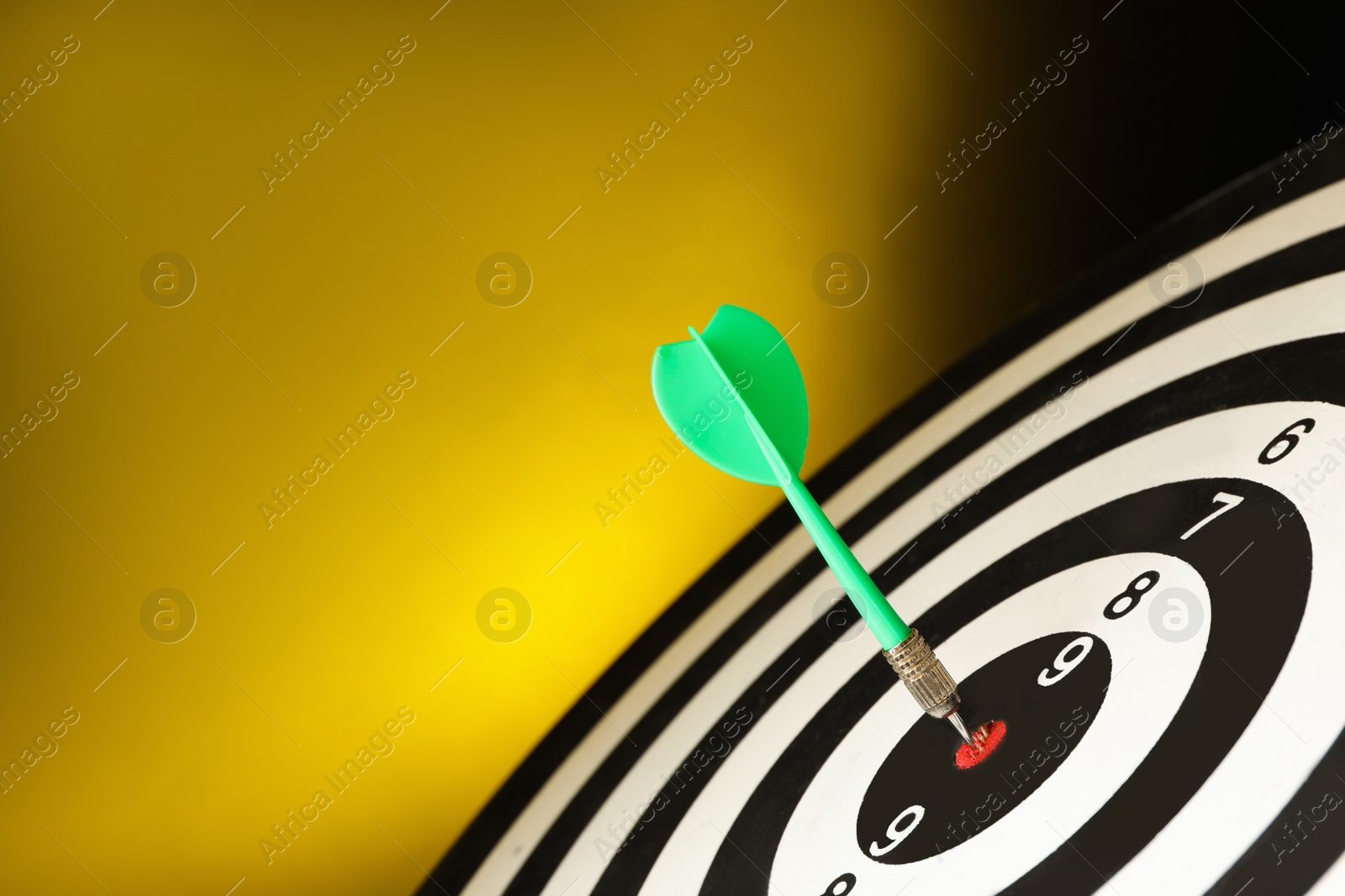 Photo of Green arrow hitting target on dart board against yellow background. Space for text