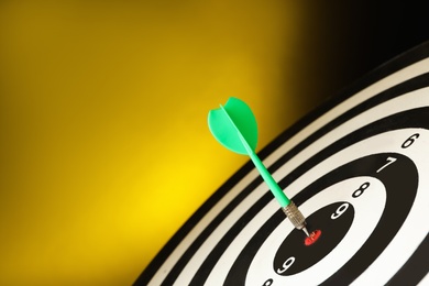 Green arrow hitting target on dart board against yellow background. Space for text