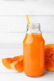 Tasty pumpkin juice in glass bottle and cut pumpkin on white wooden table
