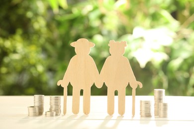 Photo of Pension savings. Figure of senior couple and stacked coins on white wooden table outdoors