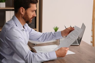 Photo of Businessman reading document at wooden table in office