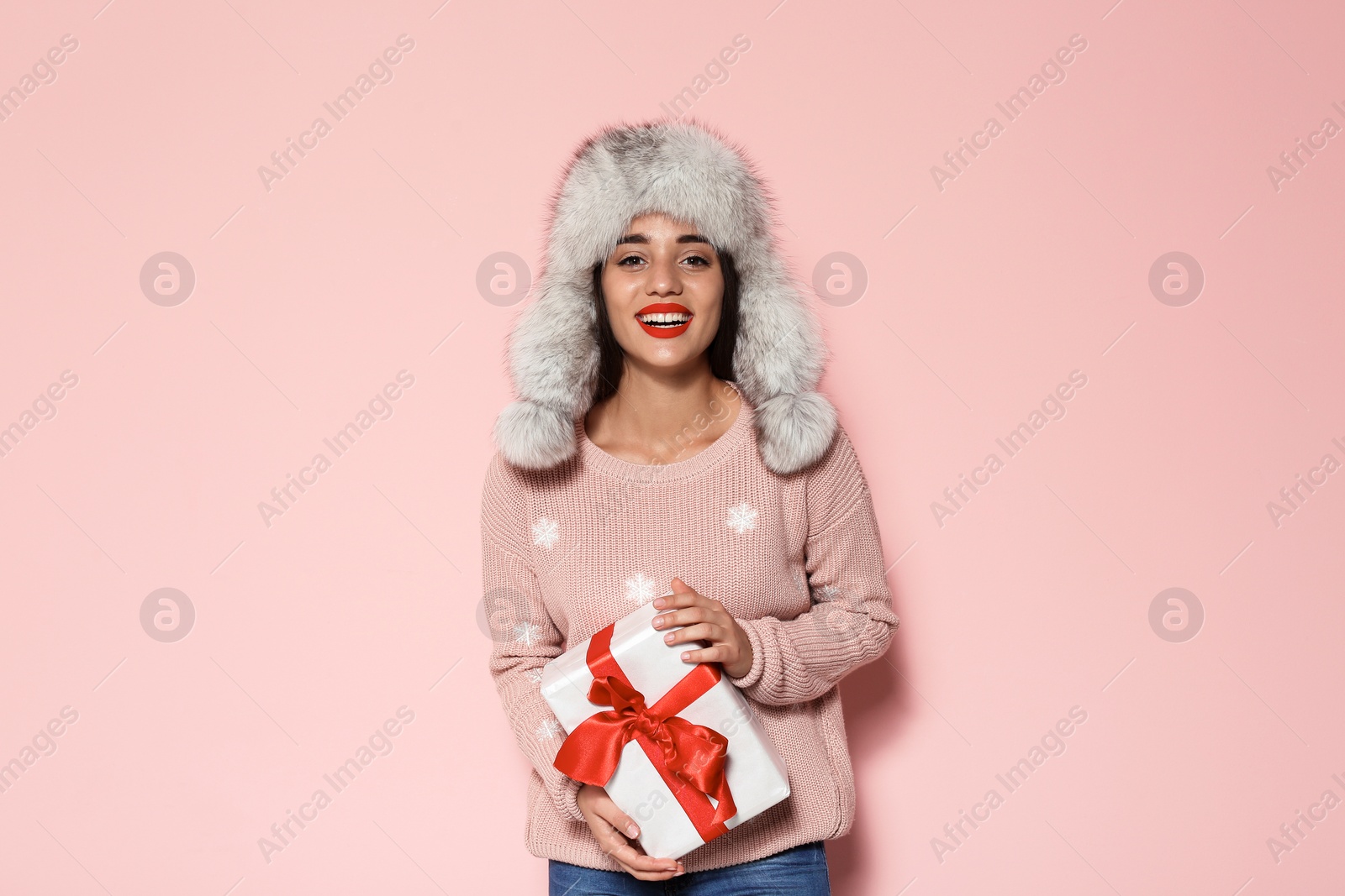 Photo of Young woman in warm sweater and hat holding Christmas gift on color background