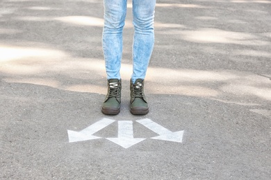 Photo of Woman standing near arrows on asphalt. Choice concept