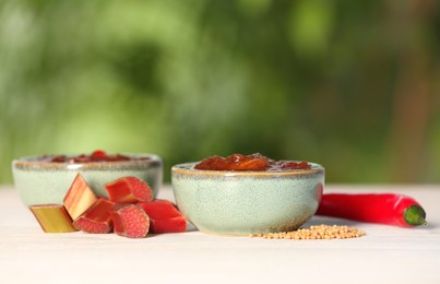 Photo of Tasty rhubarb sauce and ingredients on white table against blurred background, closeup. Space for text