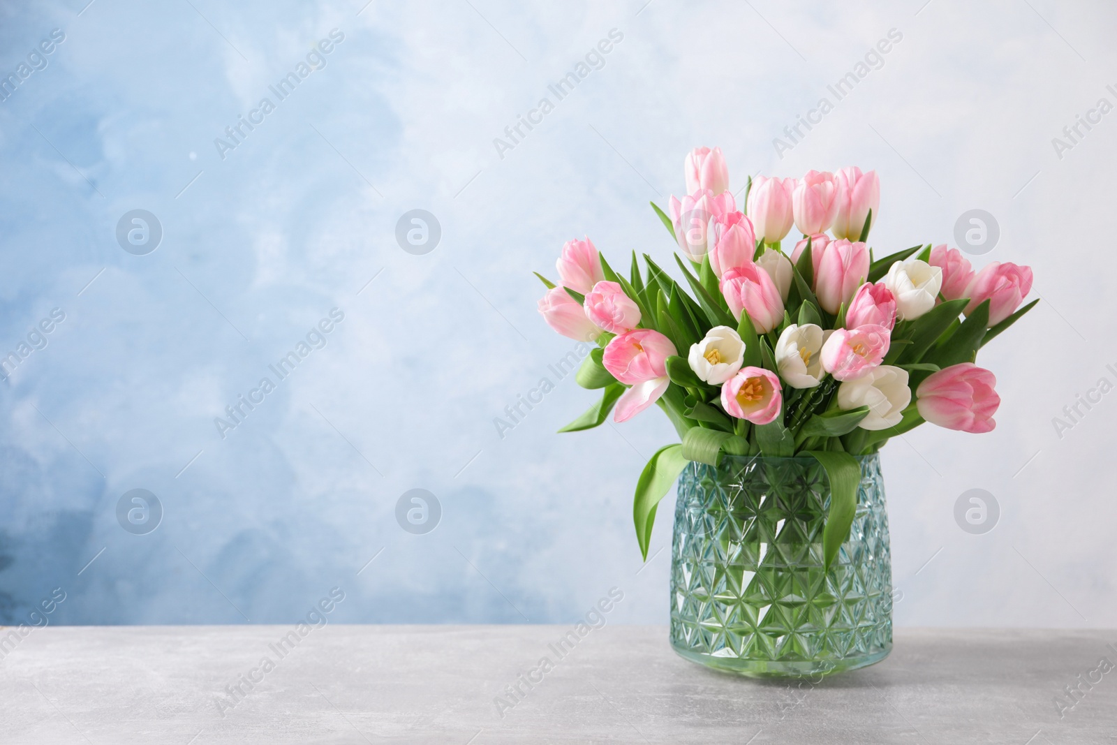 Photo of Beautiful bouquet of tulips in glass vase on light table. Space for text