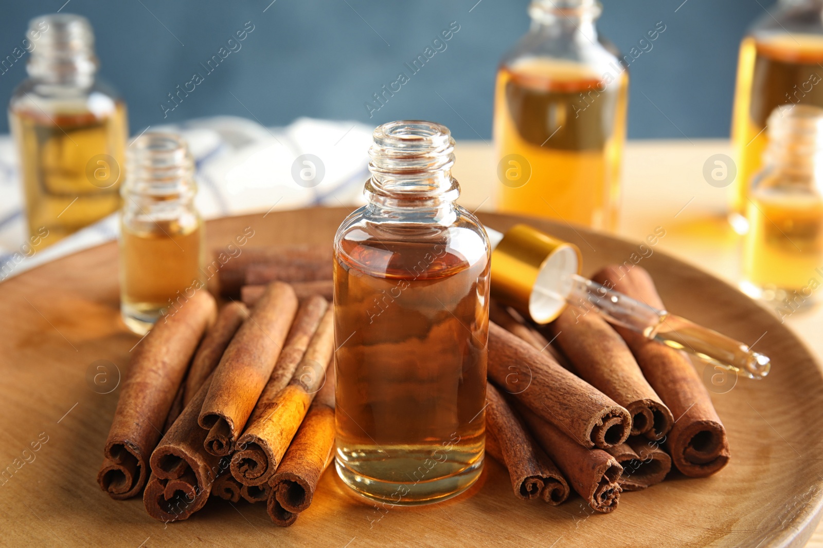 Photo of Bottles of essential oils and cinnamon sticks on wooden plate, closeup