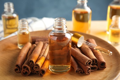 Photo of Bottles of essential oils and cinnamon sticks on wooden plate, closeup