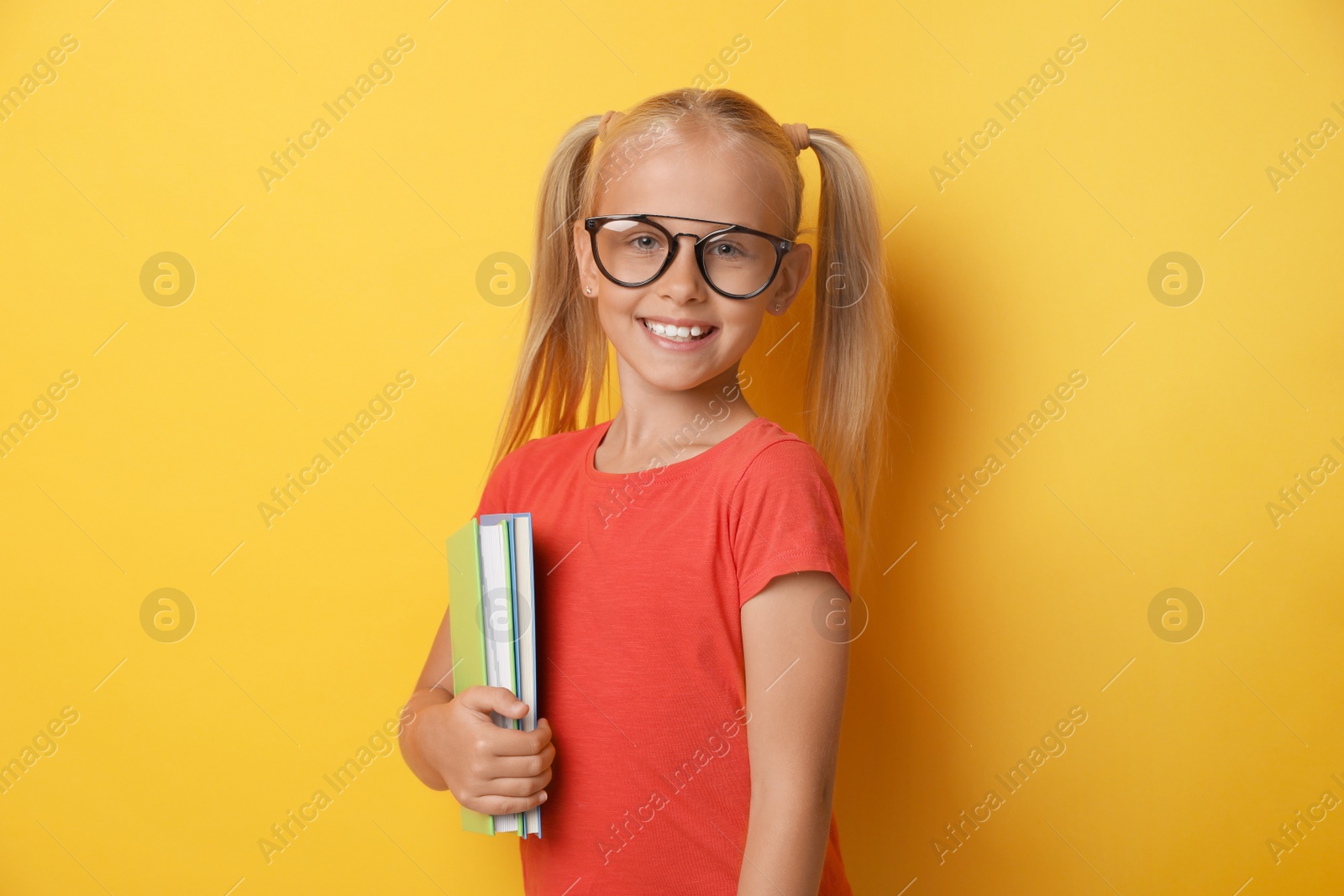 Photo of Cute little girl with glasses and books on yellow background. Reading concept