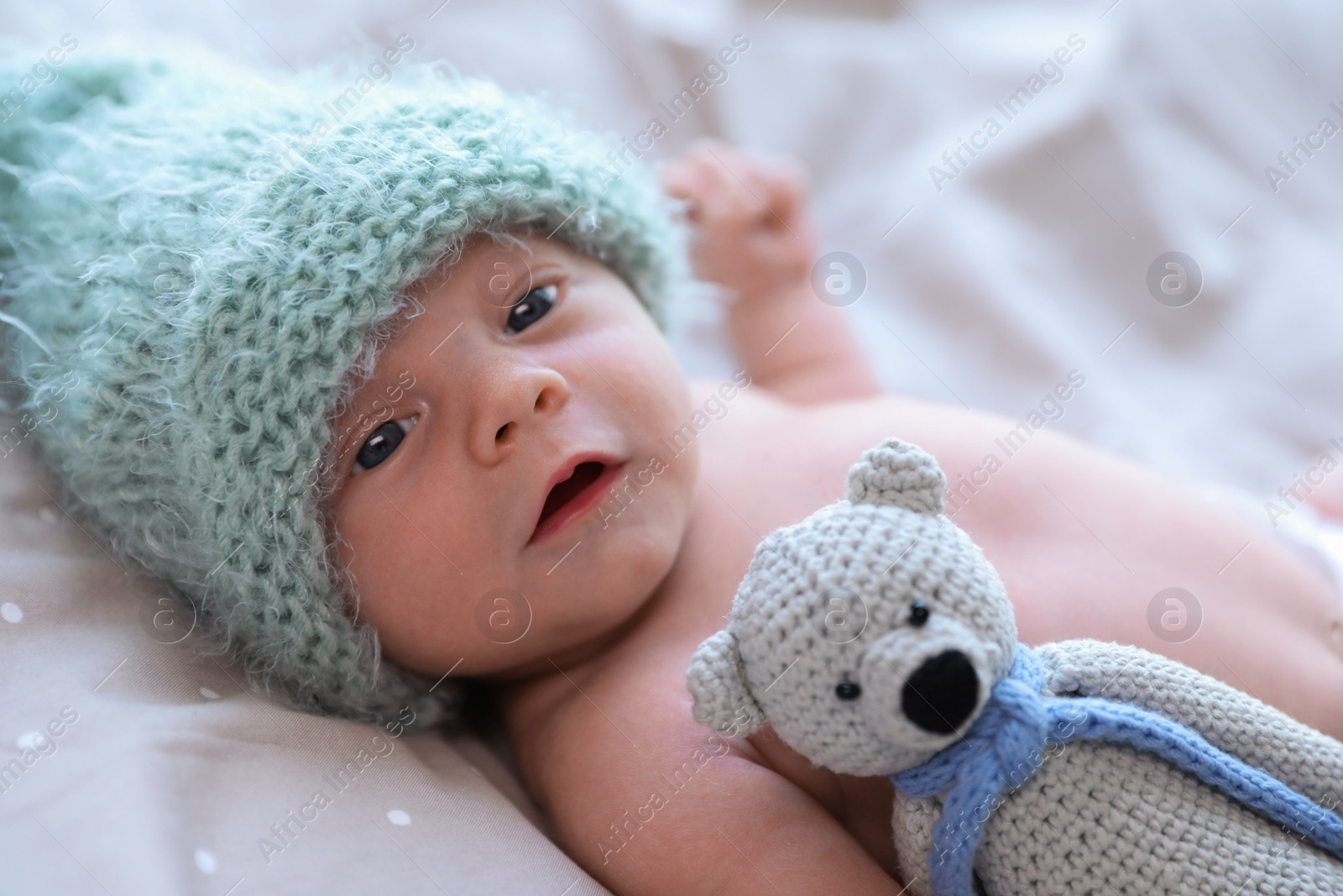Photo of Cute newborn baby in warm hat with toy lying on bed