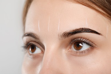 Woman during eyebrow tinting procedure on grey background, closeup