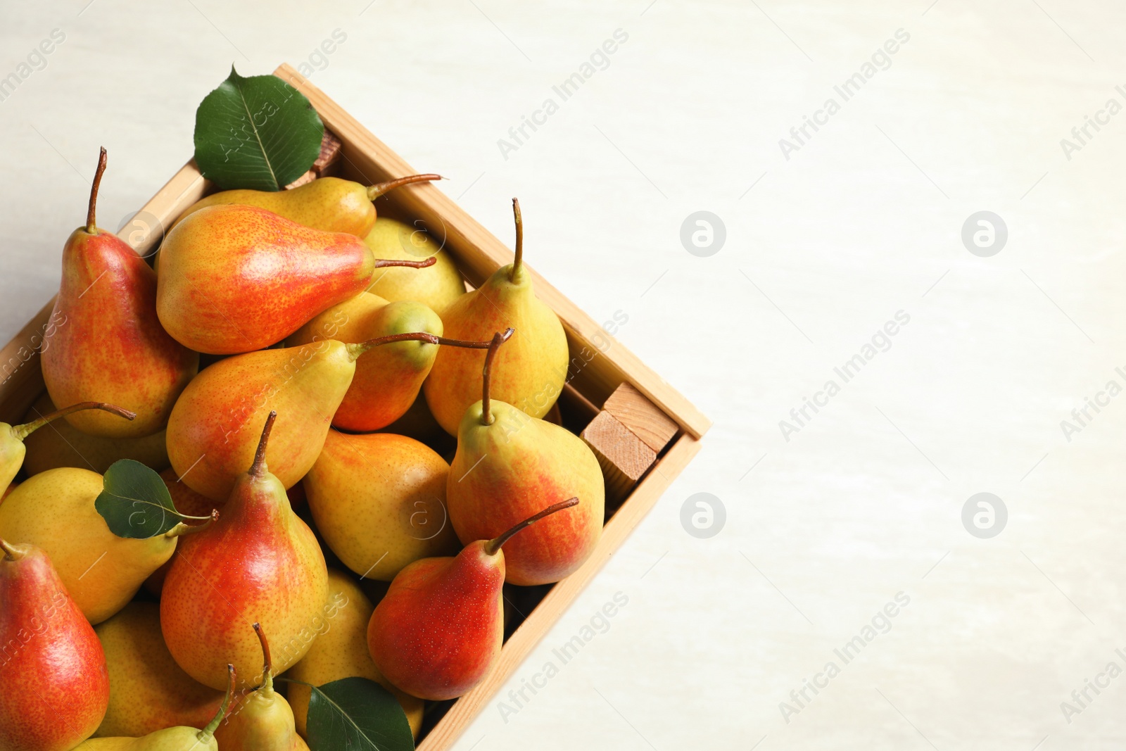 Photo of Wooden crate with ripe pears on light background, top view. Space for text