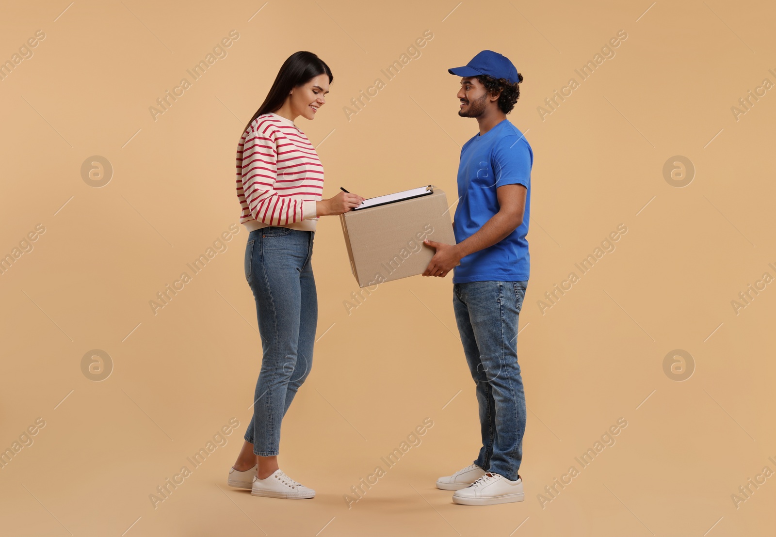 Photo of Smiling woman signing order receipt on light brown background. Courier delivery