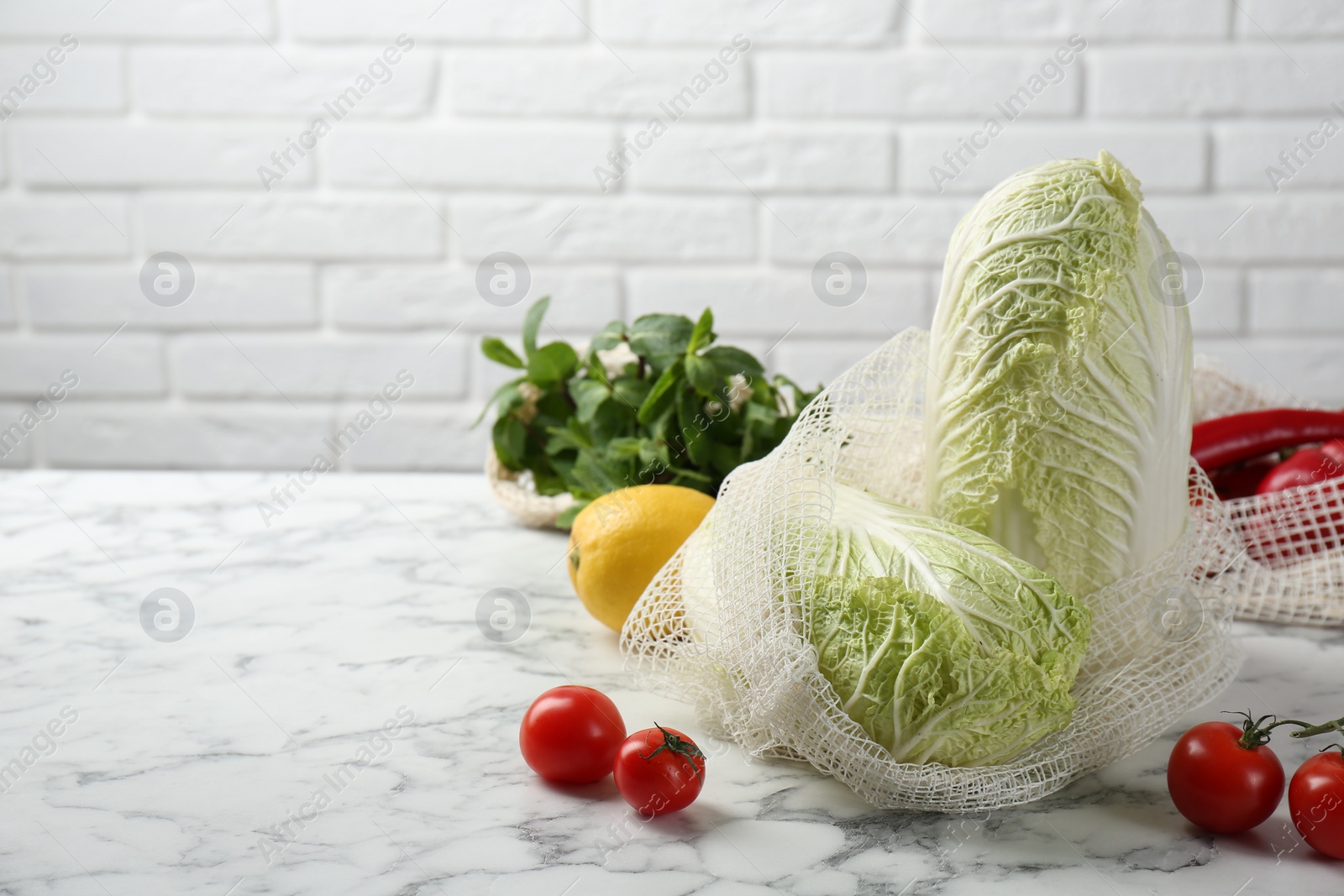 Photo of Fresh Chinese cabbages and other vegetables on white marble table near brick wall. Space for text