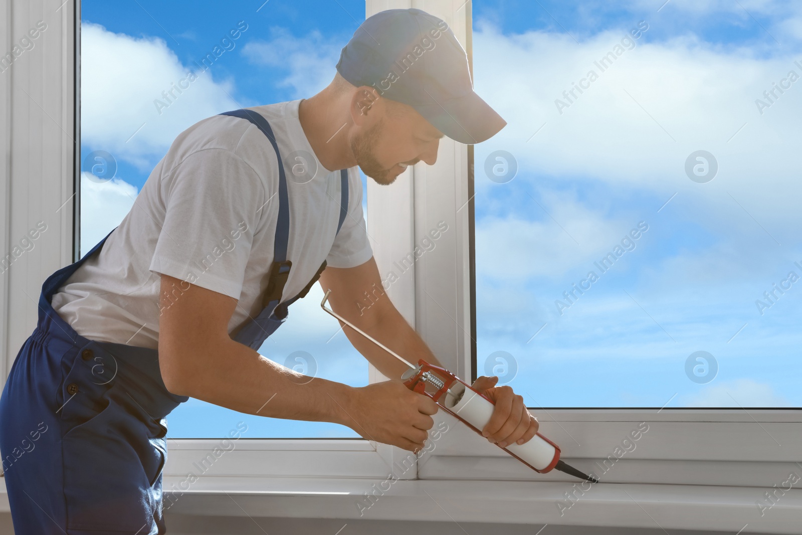 Photo of Worker sealing plastic window with caulk indoors. Installation process