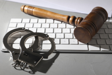 Photo of Gavel, handcuffs and computer keyboard on grey table. Cyber crime
