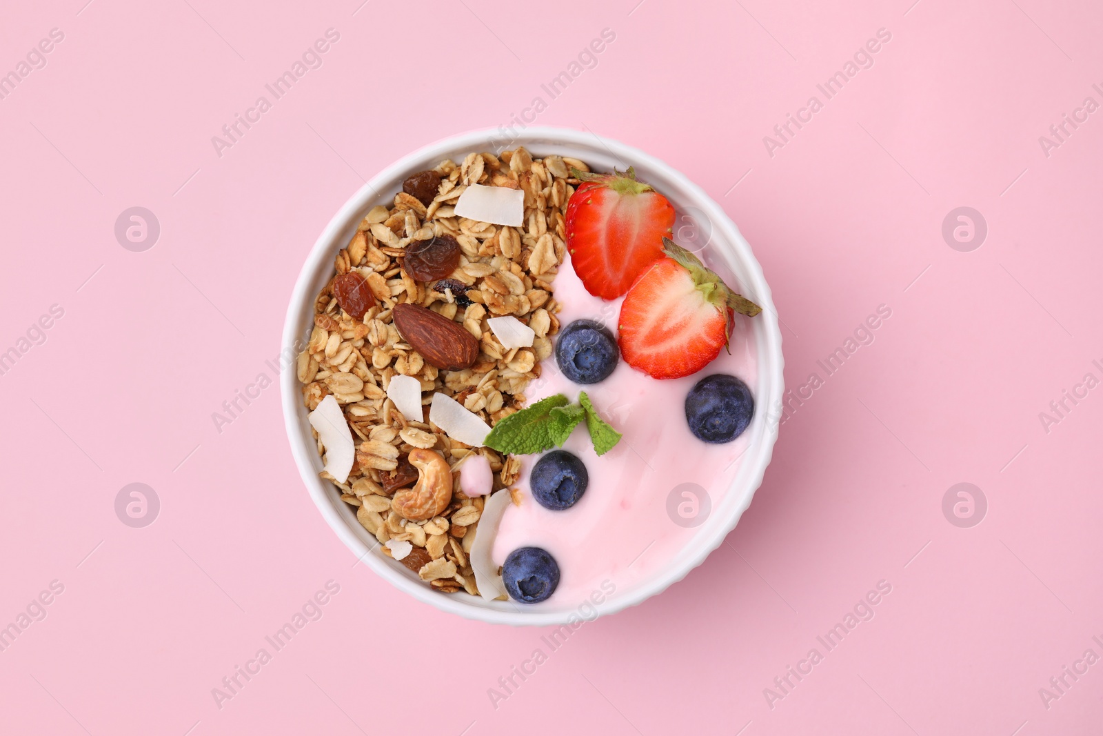 Photo of Tasty granola, yogurt and fresh berries in bowl on pink background, top view. Healthy breakfast